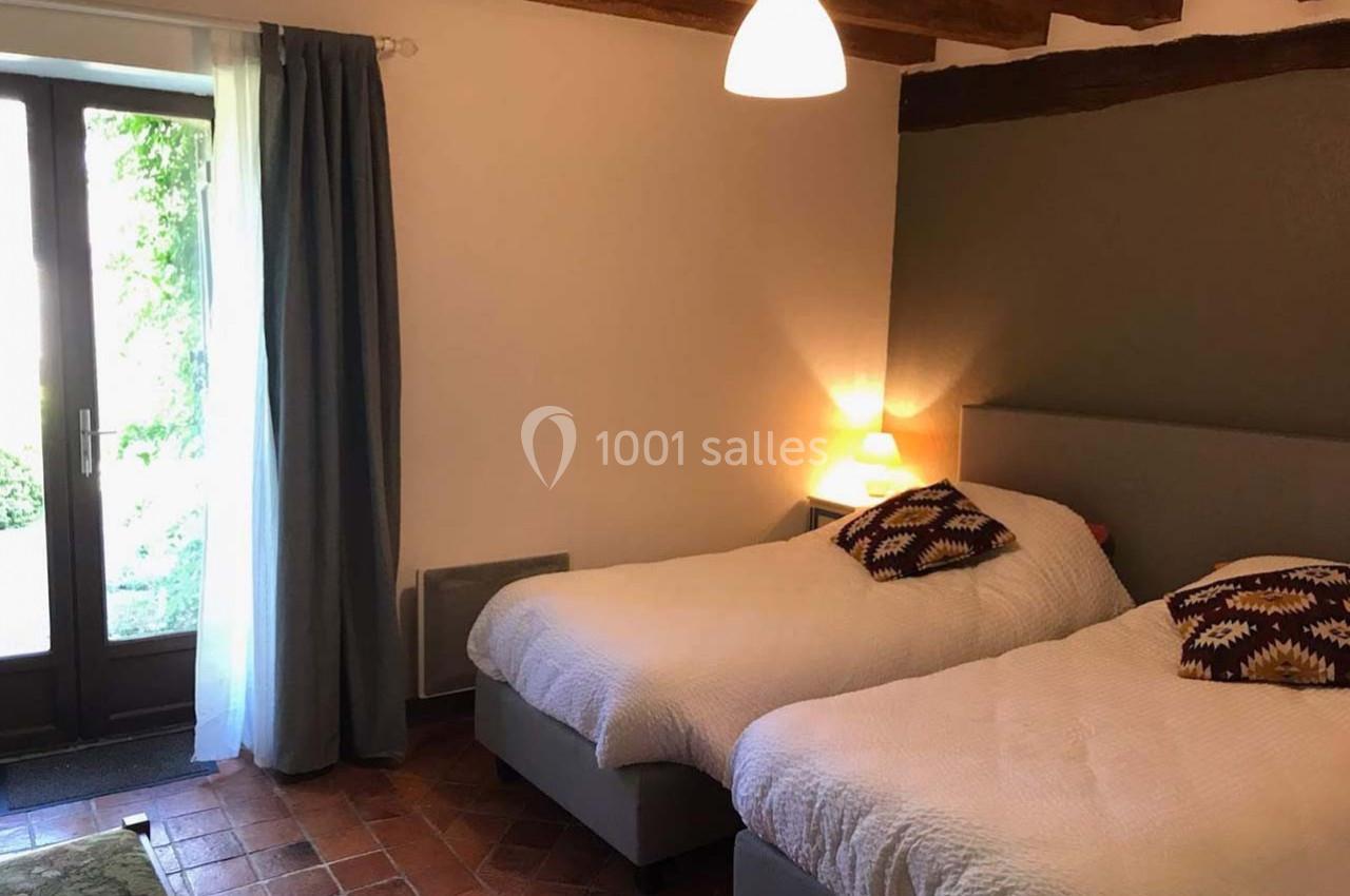 Deux lits simples avec couvre-lits blancs dans une chambre lumineuse avec sol en terre cuite et poutres apparentes.