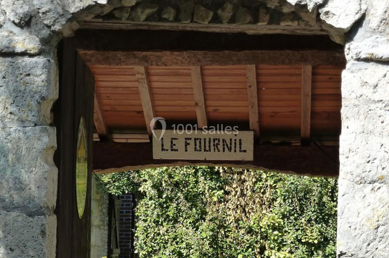 Entrée voûtée en pierre avec un panneau en bois indiquant ’Le Fournil’, entourée de végétation.