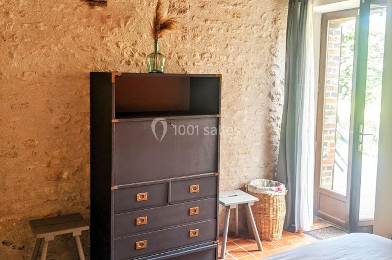 Commode noire avec tiroirs et étagères, entourée de tabourets, près d'une porte-fenêtre donnant sur un extérieur verdoyant.