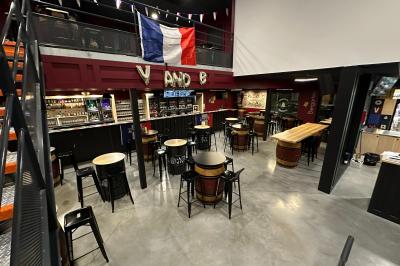 Un homme pose dans un magasin de boissons, tenant deux bouteilles devant un présentoir de bières variées.