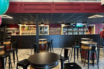Un homme pose dans un magasin de boissons, tenant deux bouteilles devant un présentoir de bières variées.