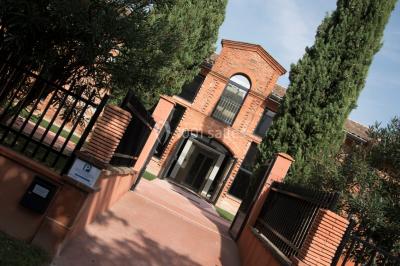 Bâtiment en briques rouges avec une allée bordée de pelouses et des drapeaux visibles au loin sous un ciel dégagé.