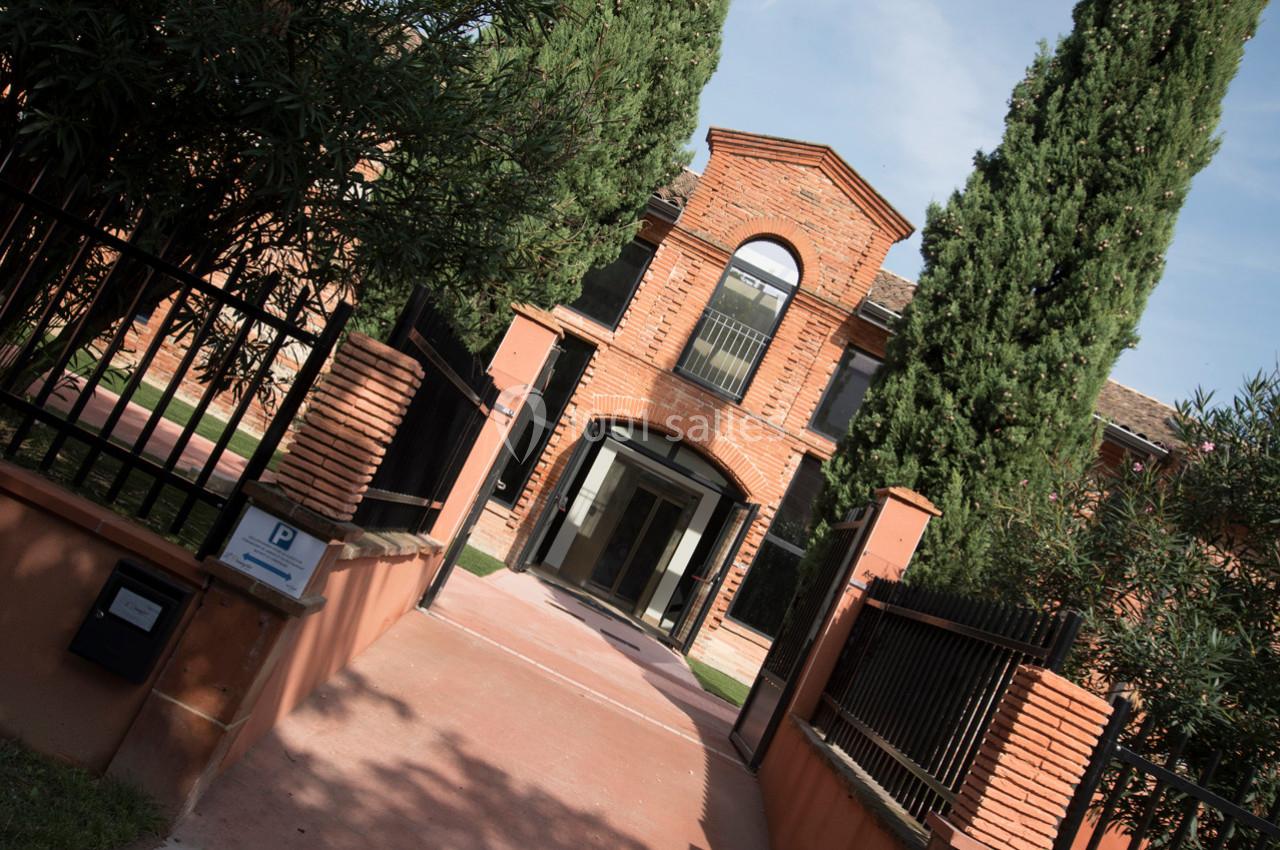 Entrée d'un bâtiment en briques rouges avec une porte vitrée, entourée d'arbres et de clôtures noires.