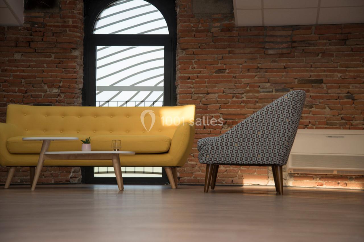 Canapé jaune et fauteuil à motifs disposés autour d'une table basse dans une pièce aux murs en briques apparentes.