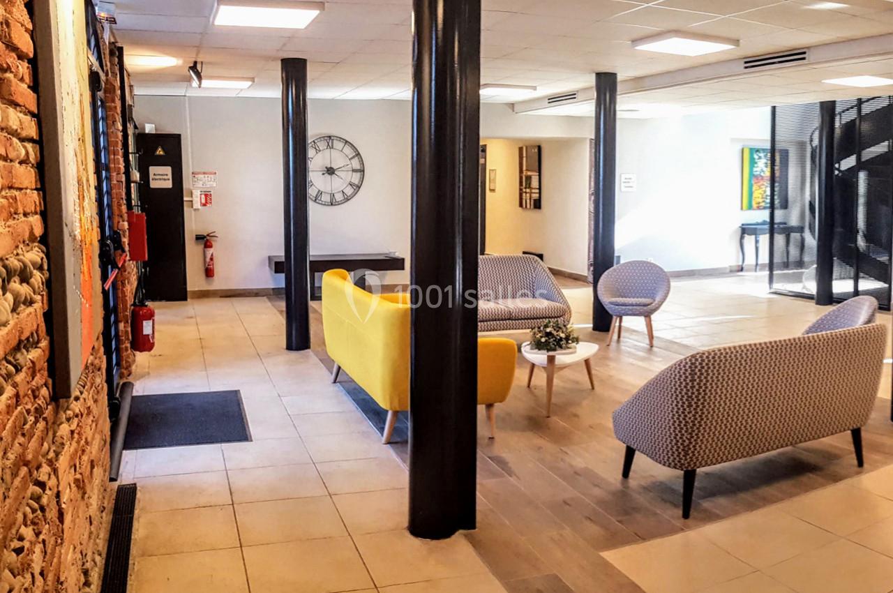 Espace de détente lumineux avec canapés colorés, tables basses et murs combinant briques et peinture claire.