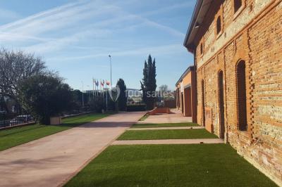 Bâtiment en briques rouges avec une allée bordée de pelouses et des drapeaux visibles au loin sous un ciel dégagé.