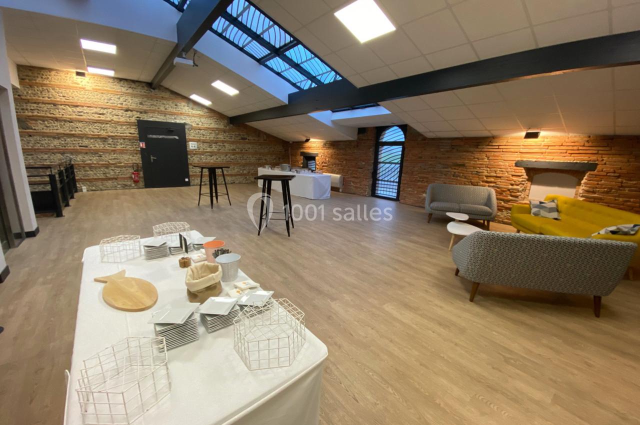 Salle lumineuse avec murs en briques, mobilier moderne, tables hautes et buffet dressé sur une nappe blanche.