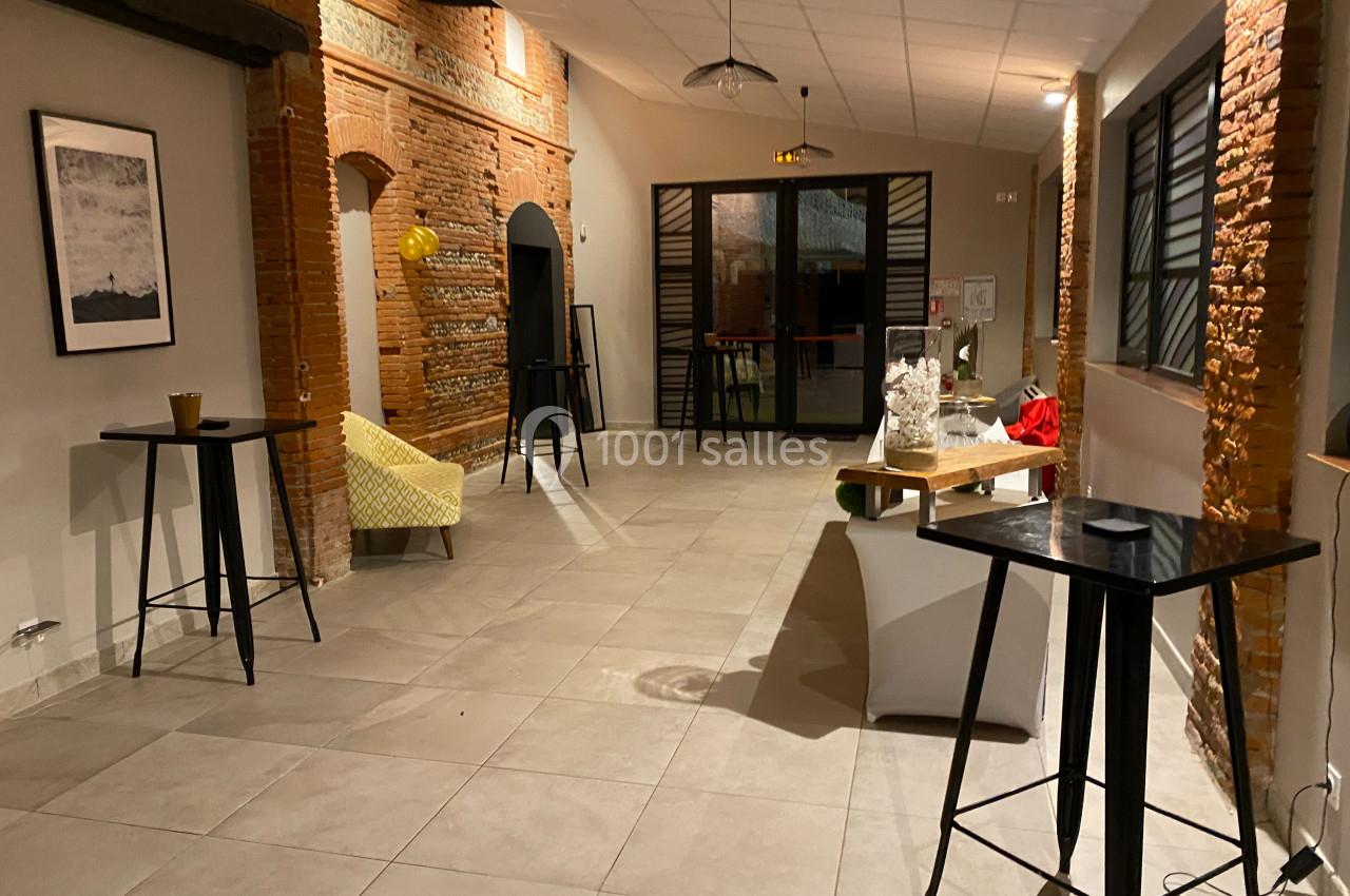 Salle lumineuse avec murs en briques, tables hautes, fauteuil jaune et décorations minimalistes.