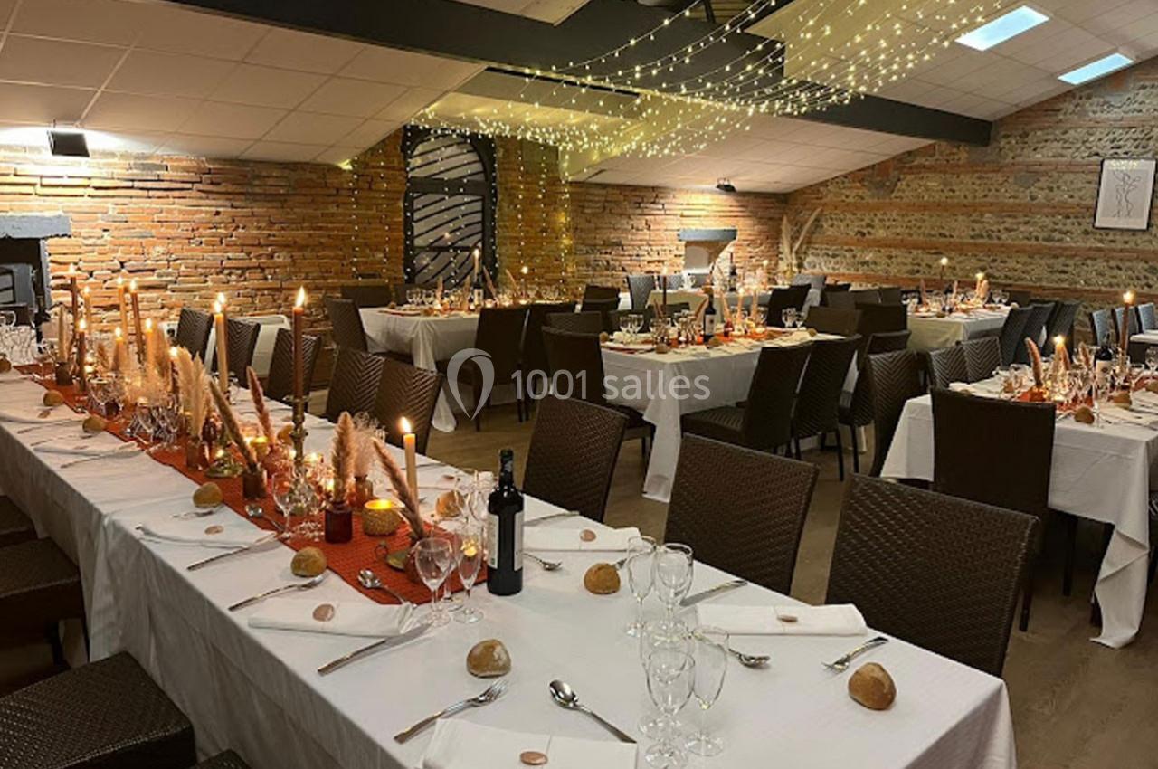 Salle de réception décorée avec des tables dressées, nappes blanches, bougies et guirlandes lumineuses au plafond.