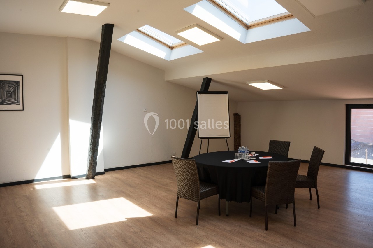 Salle lumineuse avec table ronde, chaises, tableau de conférence et puits de lumière dans un espace au design épuré.