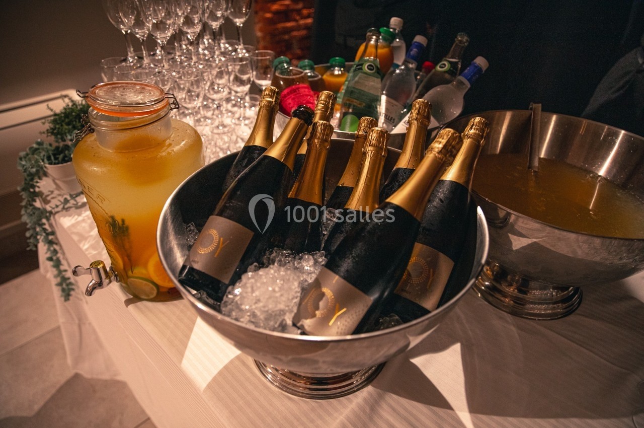 Bouteilles de champagne sur glace dans un seau, entourées de boissons variées et d'un distributeur de jus.