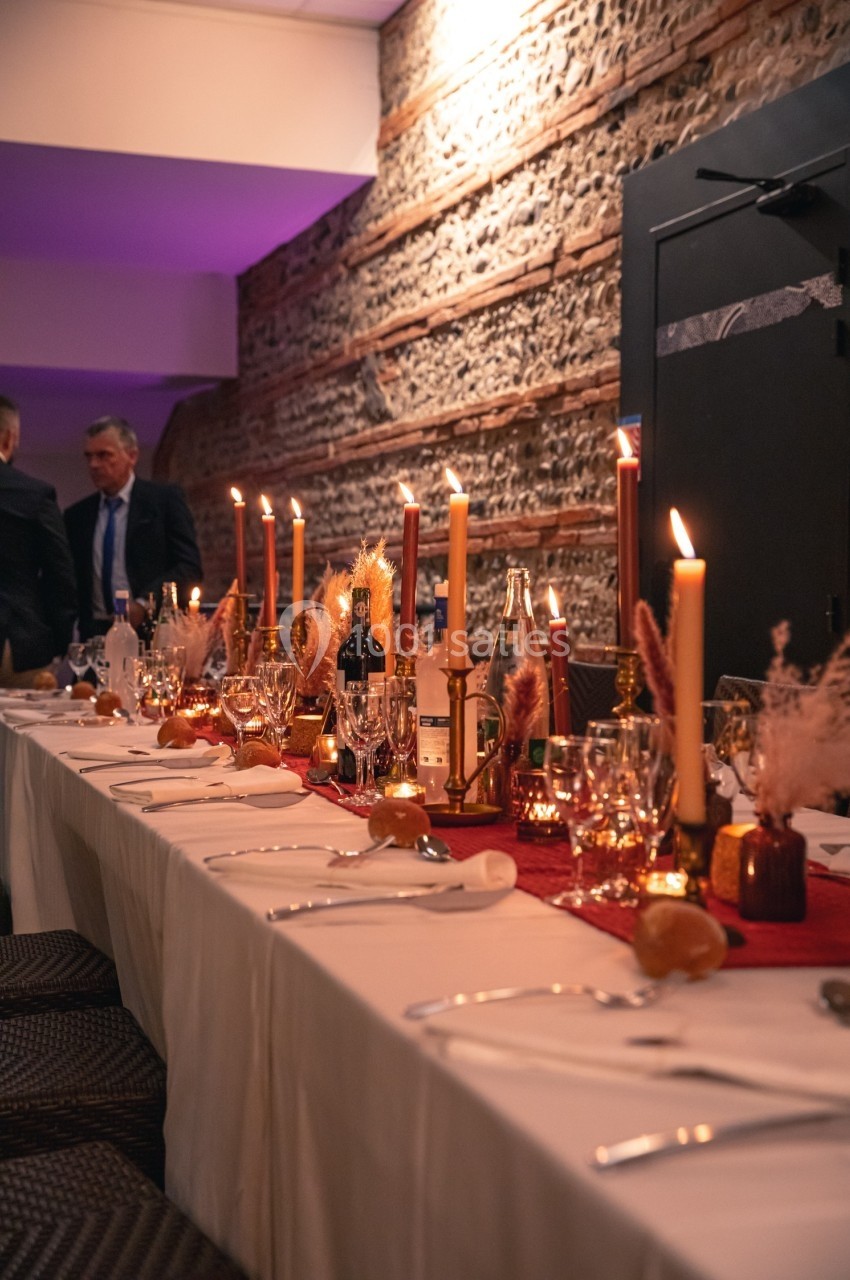 Table élégamment dressée avec bougies allumées, décoration automnale et mur en briques en arrière-plan.