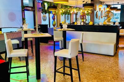 Salle de bar avec tables hautes, chaises, éclairage coloré et jeux de lumière dans une ambiance nocturne.