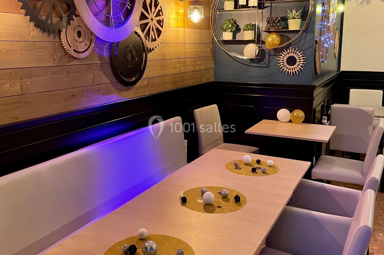 Salle de restaurant décorée avec des engrenages muraux, des plantes et des tables dressées avec des éléments décoratifs.