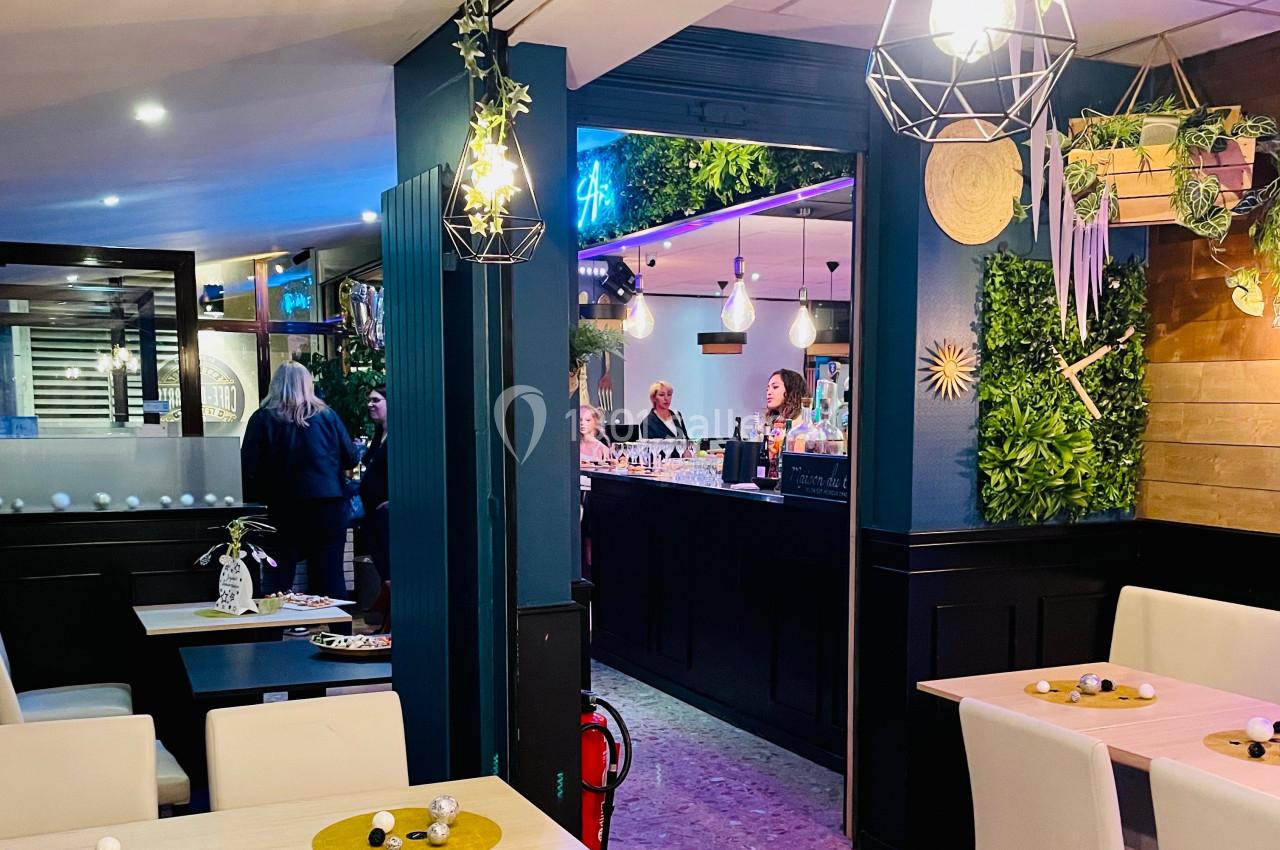 Intérieur d'un restaurant avec des tables dressées au premier plan et un bar animé en arrière-plan.