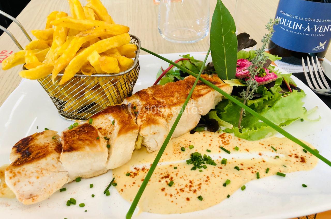 Assiette composée d'une brochette de poulet, frites dans un panier, salade verte et sauce, avec une bouteille de vin en…