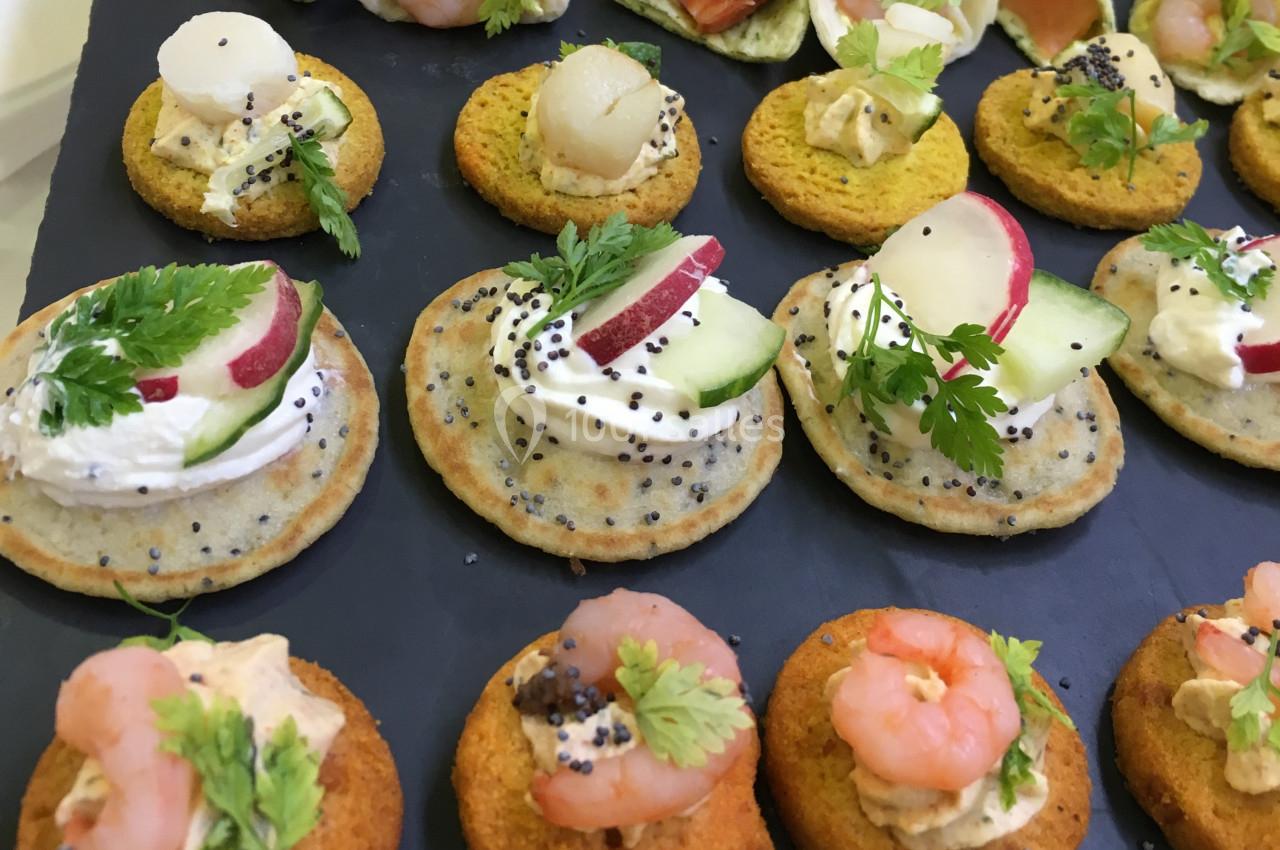 Assortiment de canapés garnis de légumes, crevettes, fromage frais et herbes, présentés sur un plateau noir.