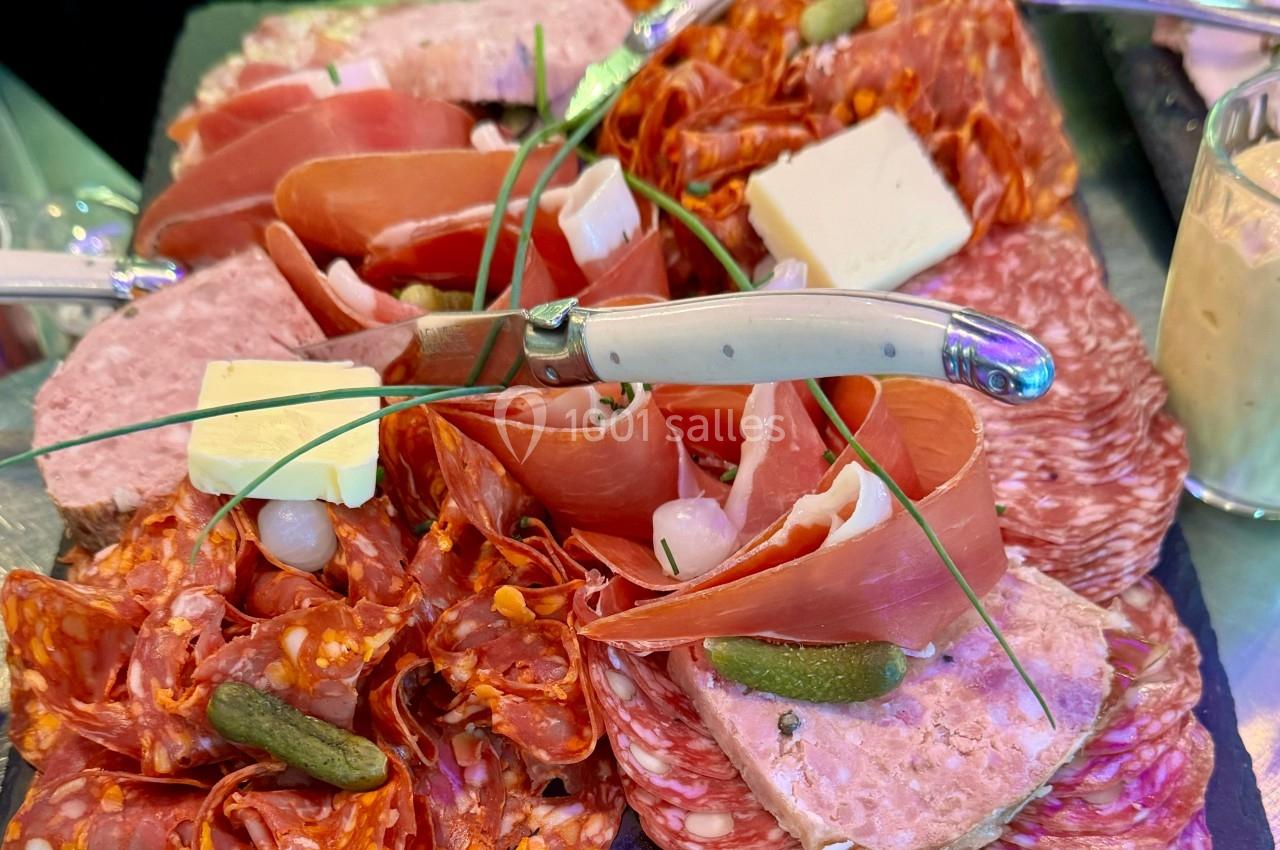 Plateau de charcuterie variée avec saucissons, jambon, pâté, cornichons, fromage et brins de ciboulette.