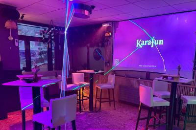 Salle de bar avec tables hautes, chaises, éclairage coloré et jeux de lumière dans une ambiance nocturne.