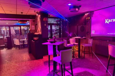 Salle de bar avec tables hautes, chaises, éclairage coloré et jeux de lumière dans une ambiance nocturne.