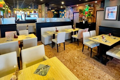 Salle de restaurant moderne avec tables dressées, chaises blanches, décoration murale et éclairage chaleureux.