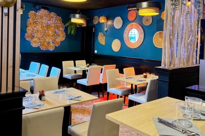 Salle de restaurant moderne avec tables dressées, chaises blanches, décoration murale et éclairage chaleureux.