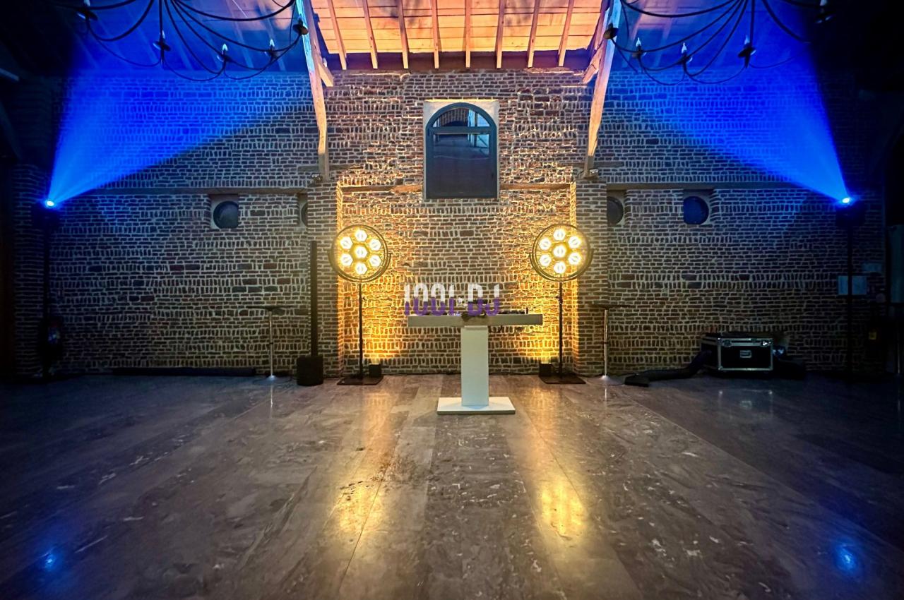 Salle en briques avec éclairage coloré, projecteurs circulaires et une table blanche au centre.