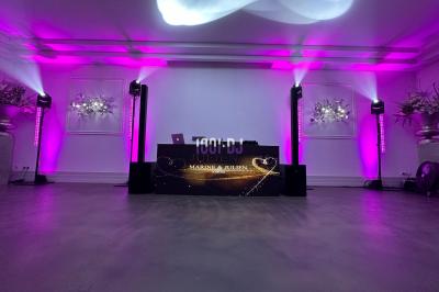 Des invités dansent sous un éclairage coloré dans une salle décorée avec des ballons suspendus et un plafond drapé.