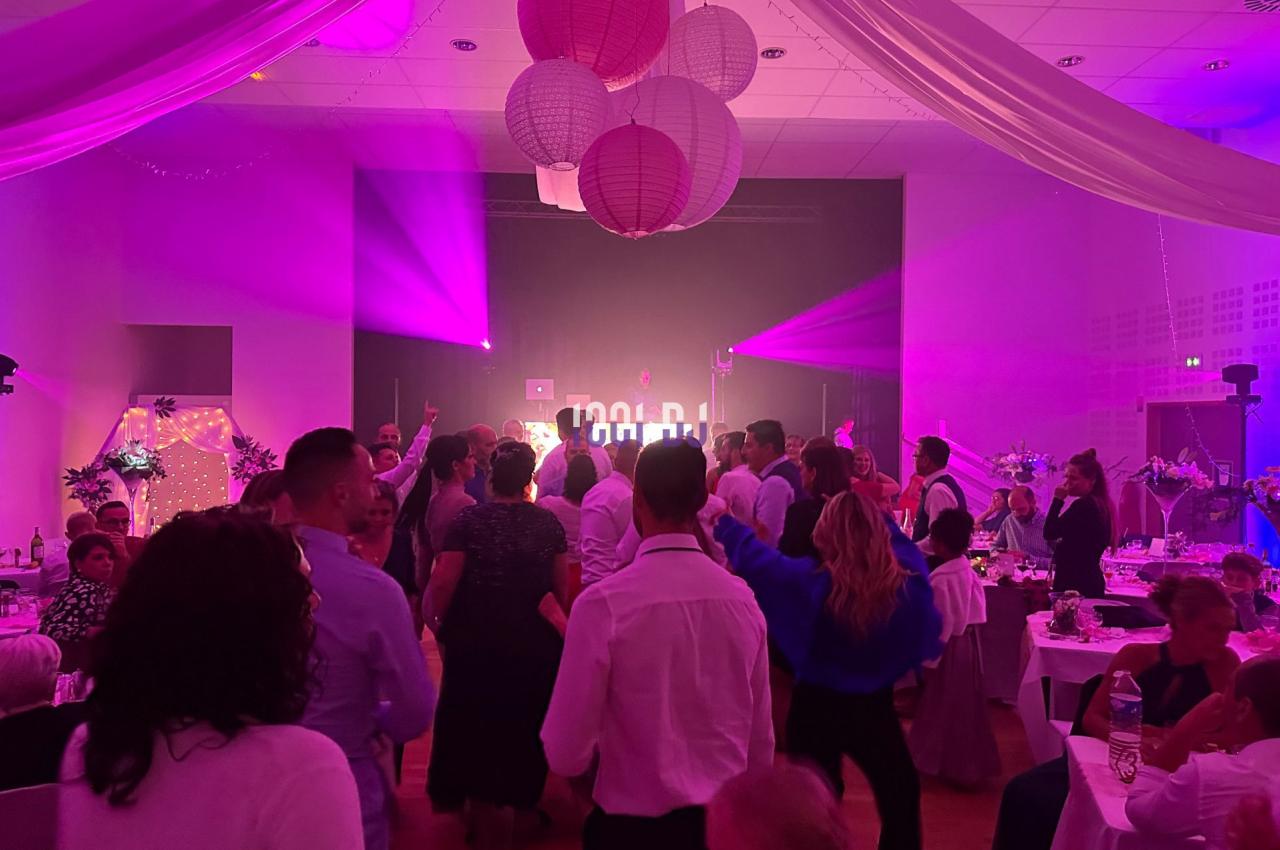 Groupe de personnes dansant dans une salle décorée avec des lanternes suspendues et éclairée par des lumières colorées.