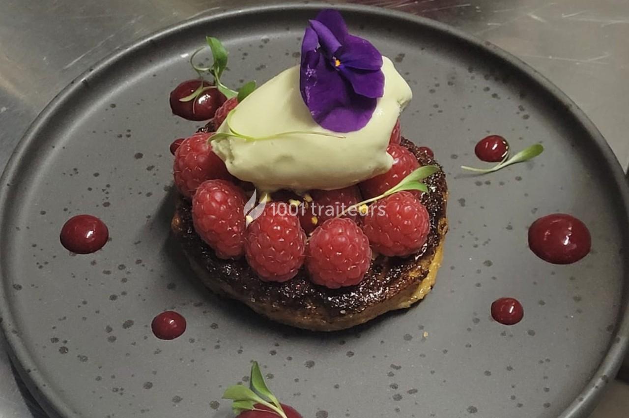 Dessert composé de framboises fraîches, glace vanille, fleur comestible violette, sur une base caramélisée.