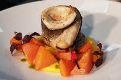 Filet de poisson roulé sur purée jaune, accompagné de morceaux de carottes et de feuilles décoratives.