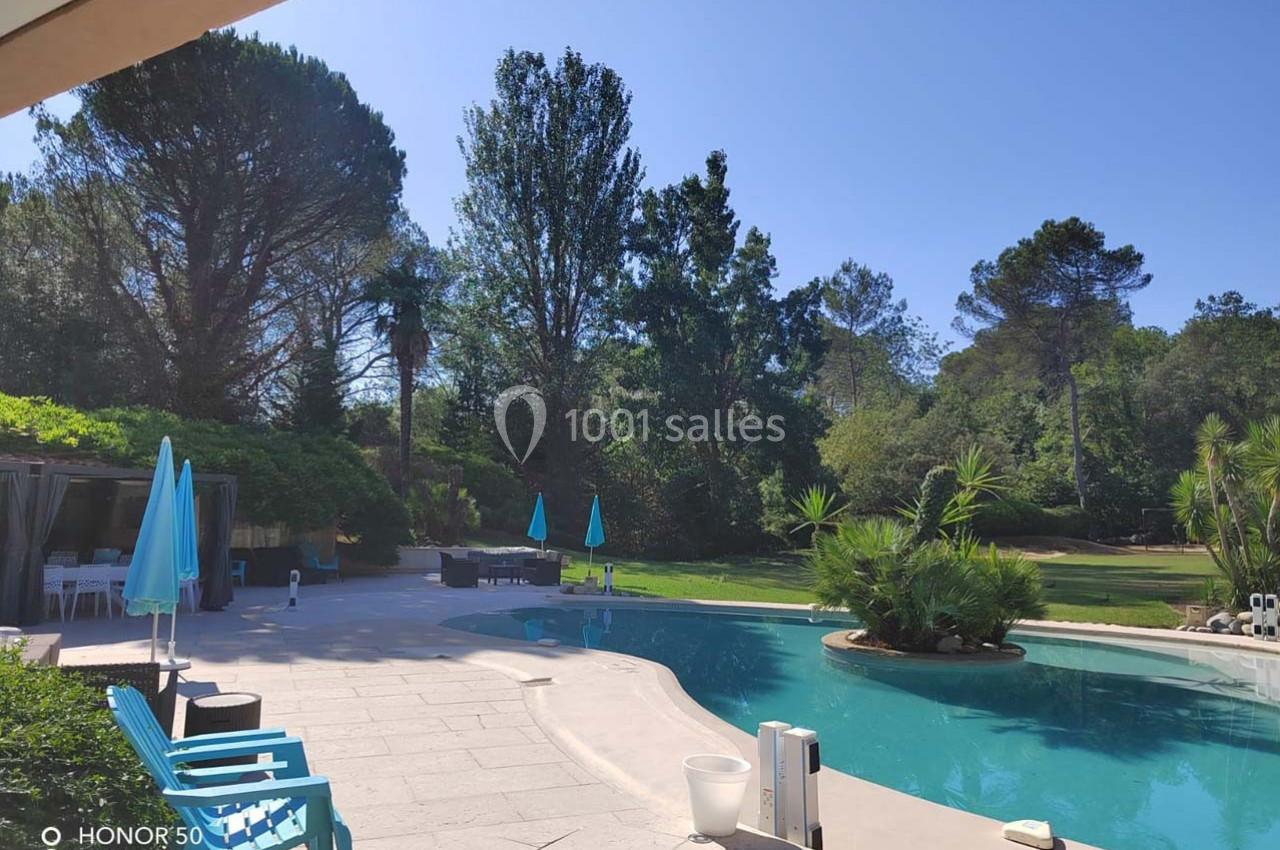 Piscine extérieure bordée de chaises et parasols bleus, entourée de végétation dense et d'arbres.