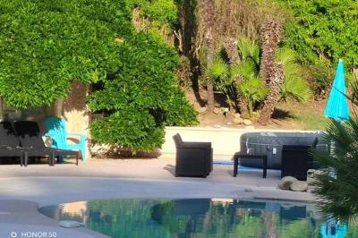 Terrasse avec table et chaises blanches sous une pergola, entourée de plantes et arbres dans un jardin ensoleillé.