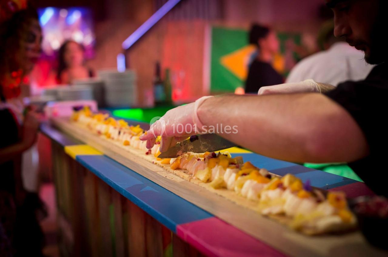 Un chef découpe un long plateau de sushis dans un environnement coloré et animé.