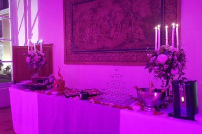 Table de buffet décorée avec des fleurs, chandeliers allumés, coupes empilées et divers plats dans une ambiance lumineuse…