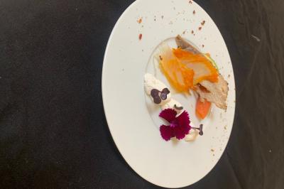 Assiette gastronomique avec légumes colorés, viande, fleurs comestibles et crème, présentée sur une nappe noire.