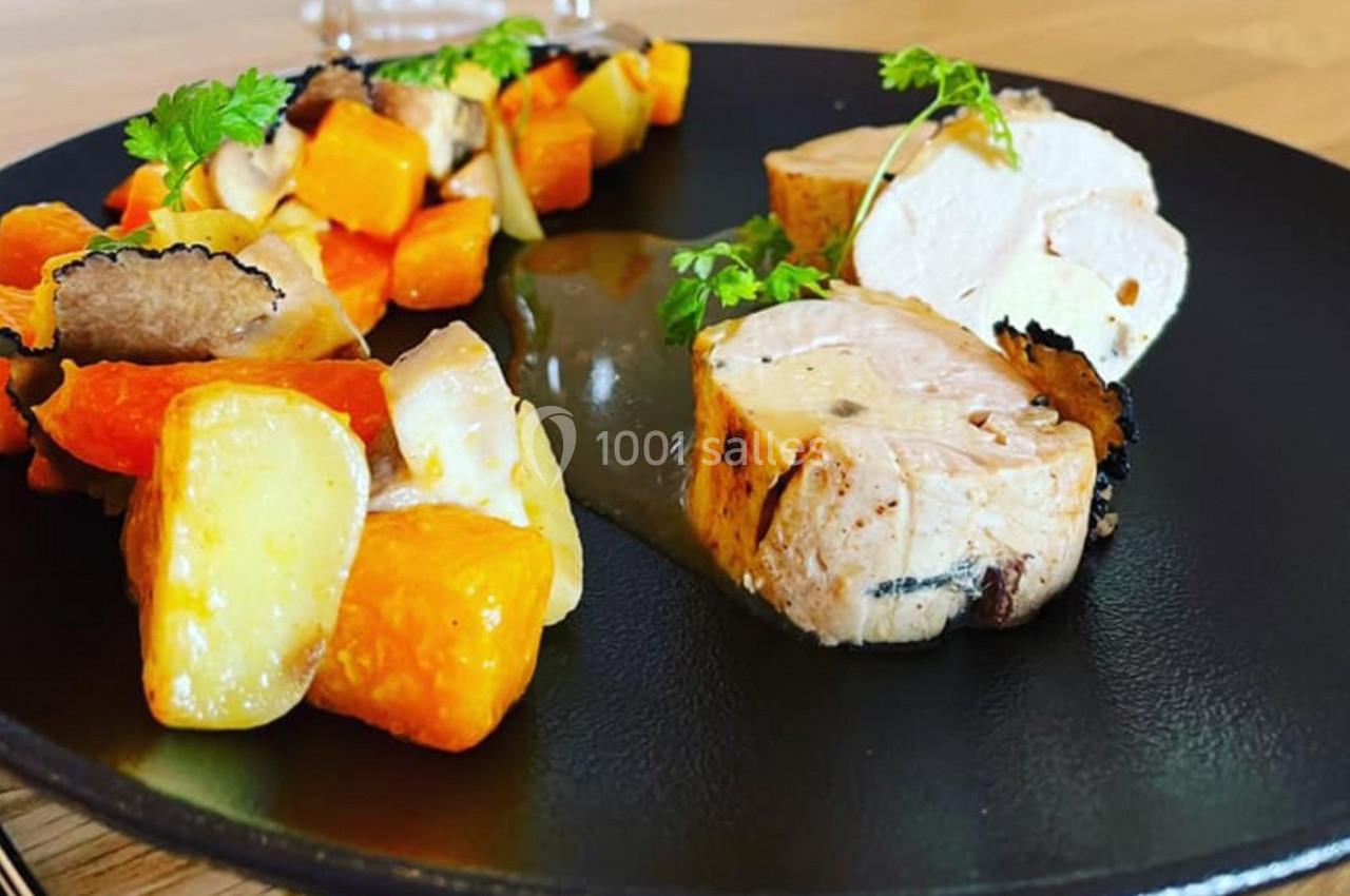 Assiette contenant des morceaux de volaille, légumes rôtis et tranches de truffe, présentée sur un plat noir.