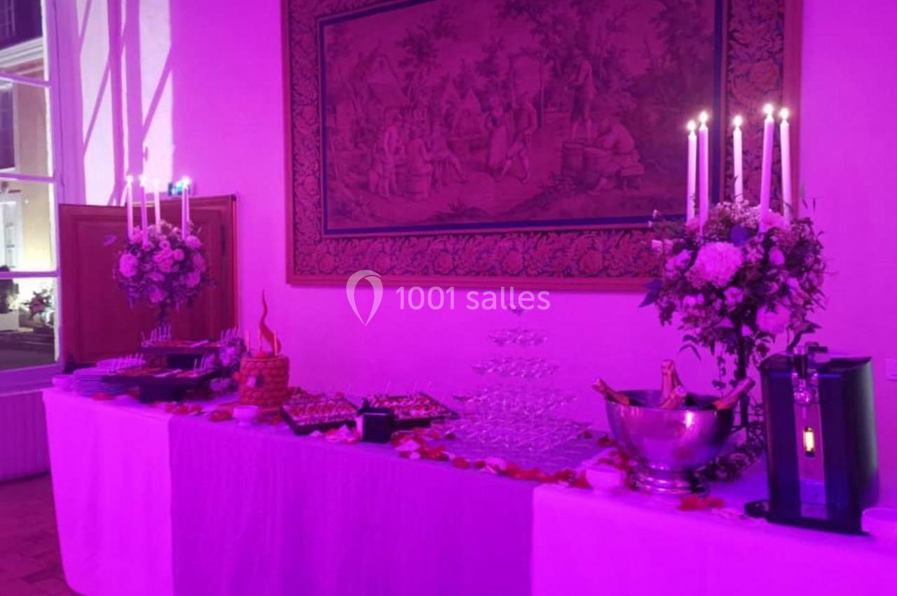 Table décorée pour un buffet avec chandeliers, fleurs, coupes empilées et divers plats dans une ambiance lumineuse violette.