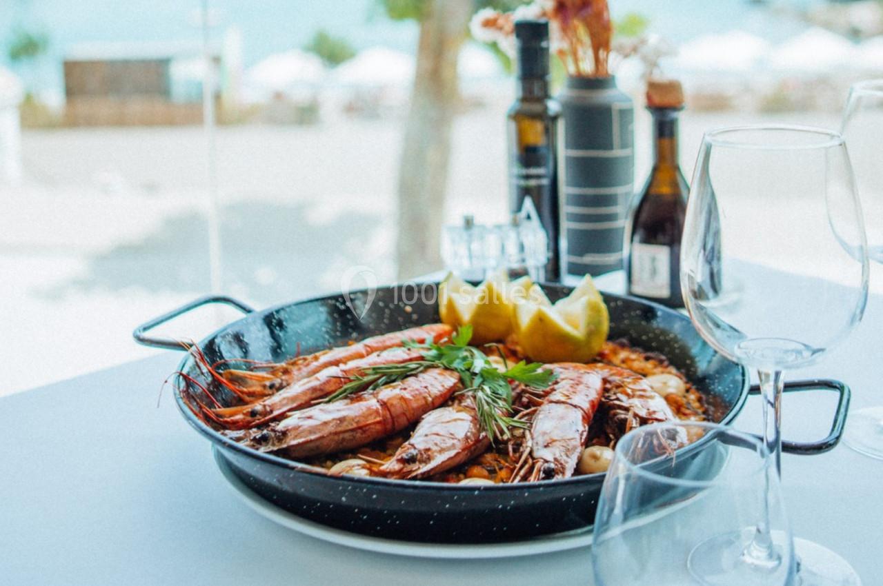 Plat de crevettes grillées servi avec des herbes et des quartiers de citron, posé sur une table en extérieur près de la mer.