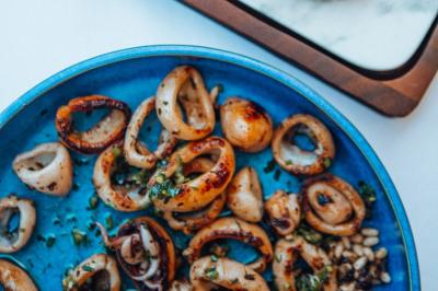 Crevettes grillées servies dans une assiette bleue avec des herbes, accompagnées de plats et d'un verre de vin rouge.