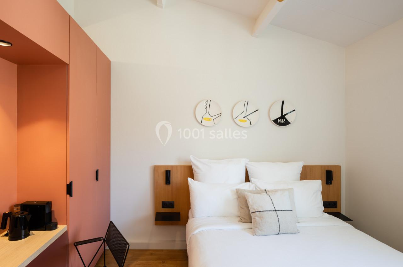 Lit double avec coussins blancs dans une chambre moderne, décorée avec des horloges murales et un placard orange.