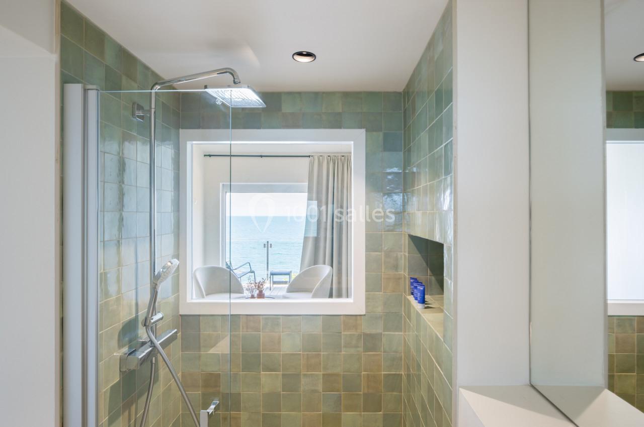 Douche avec carrelage vert, niche murale, et fenêtre donnant sur une vue dégagée de la mer.