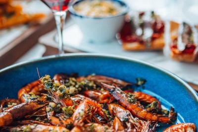 Crevettes grillées servies dans une assiette bleue avec des herbes, accompagnées de plats et d'un verre de vin rouge.