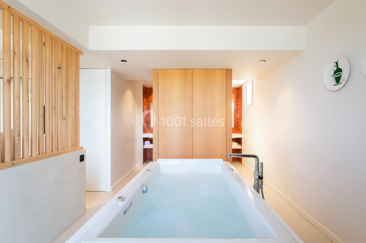 Baignoire à remous dans une salle lumineuse avec parois en bois, placards en bois clair et mur décoratif orange.