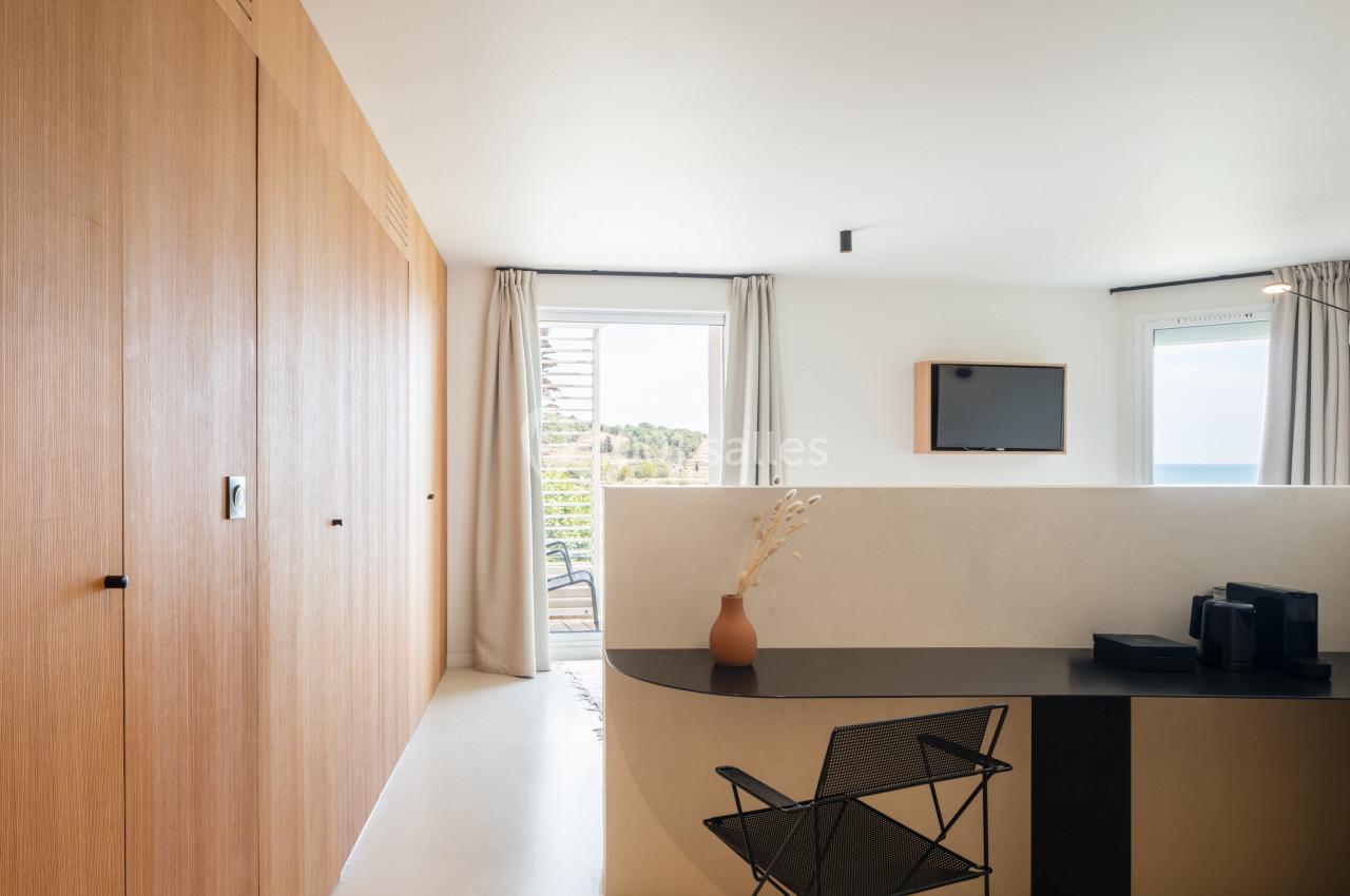 Bureau moderne avec chaise en métal, vase décoratif, et vue sur l'extérieur à travers des fenêtres avec rideaux clairs.