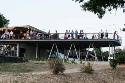 Salle lumineuse avec tables dressées pour un repas, chaises rouges, lampes suspendues et personnes en arrière-plan.