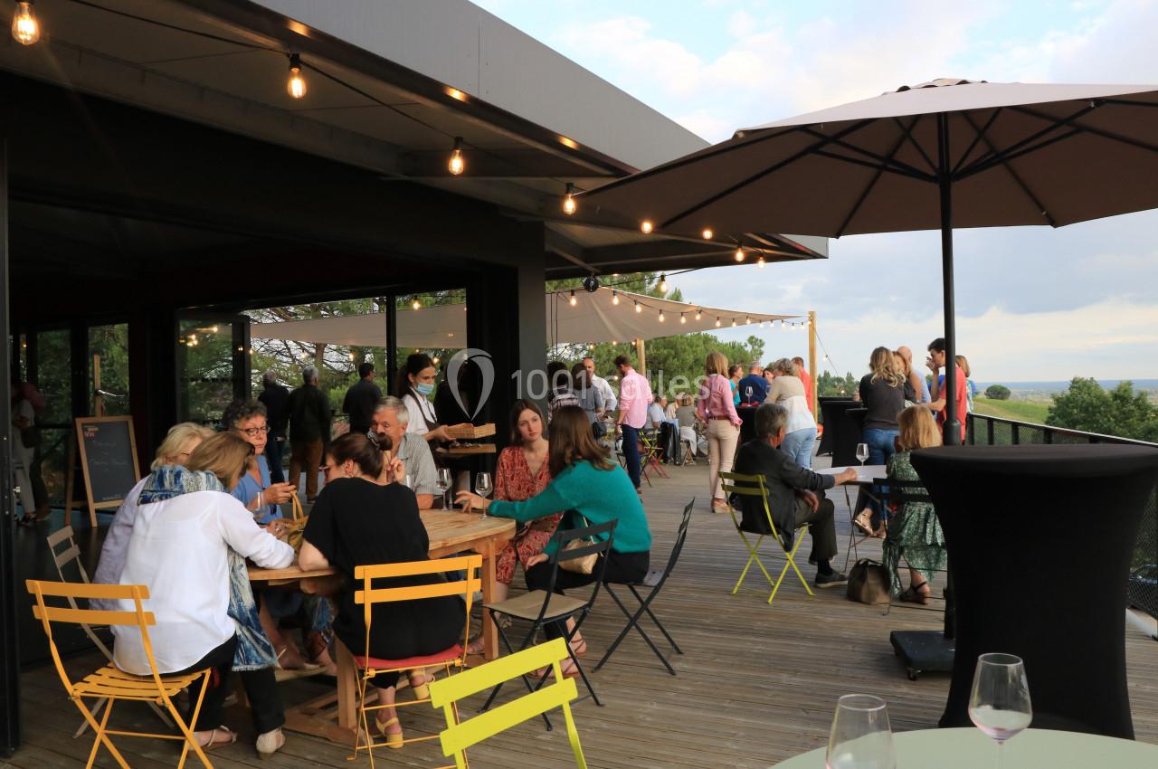 Personnes réunies sur une terrasse en bois, discutant et partageant un moment convivial sous des guirlandes lumineuses.