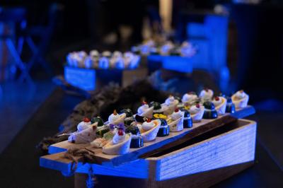 Salle lumineuse avec tables dressées pour un repas, chaises rouges, lampes suspendues et personnes en arrière-plan.