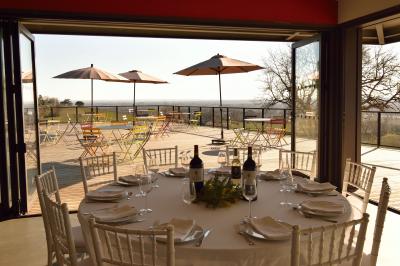Salle lumineuse avec tables dressées pour un repas, chaises rouges, lampes suspendues et personnes en arrière-plan.