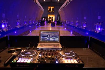 Salle lumineuse avec tables dressées pour un repas, chaises rouges, lampes suspendues et personnes en arrière-plan.